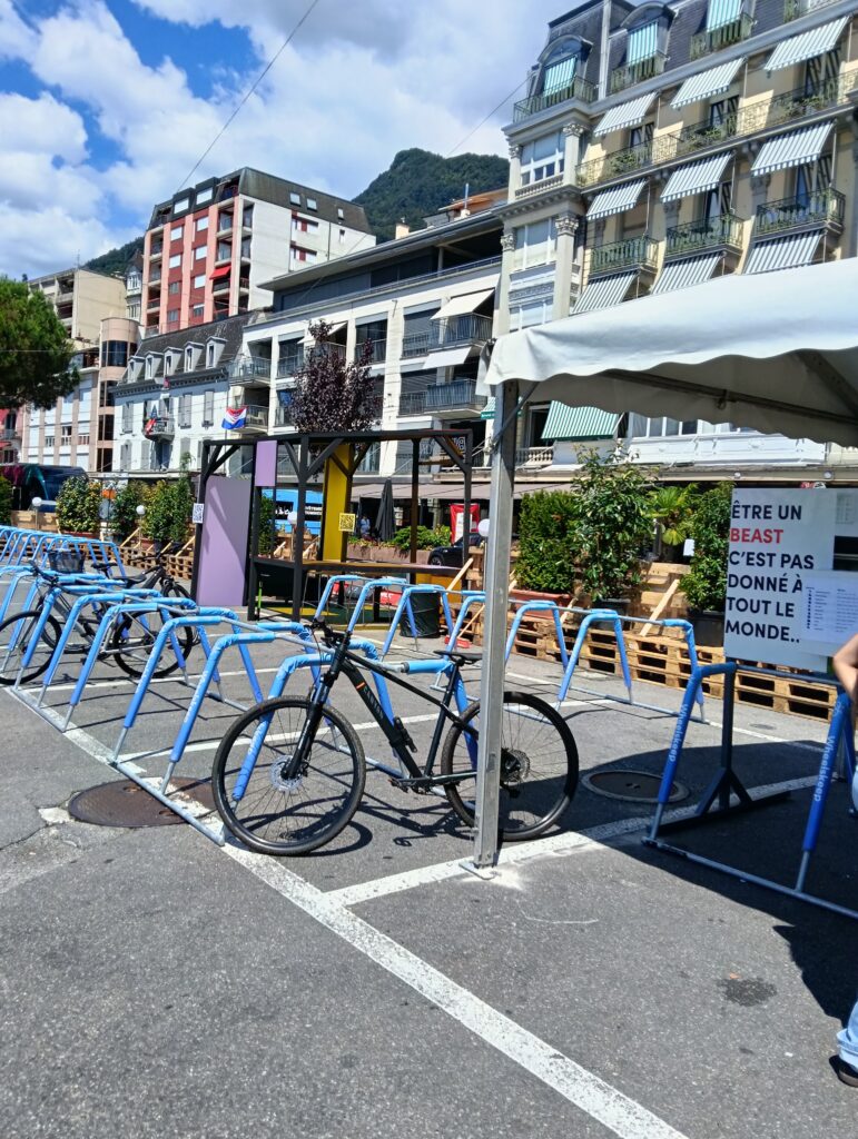 Fila de bicicletas de color azul brillante aparcadas en un portabicicletas en una soleada plaza urbana con edificios de apartamentos y una colina al fondo